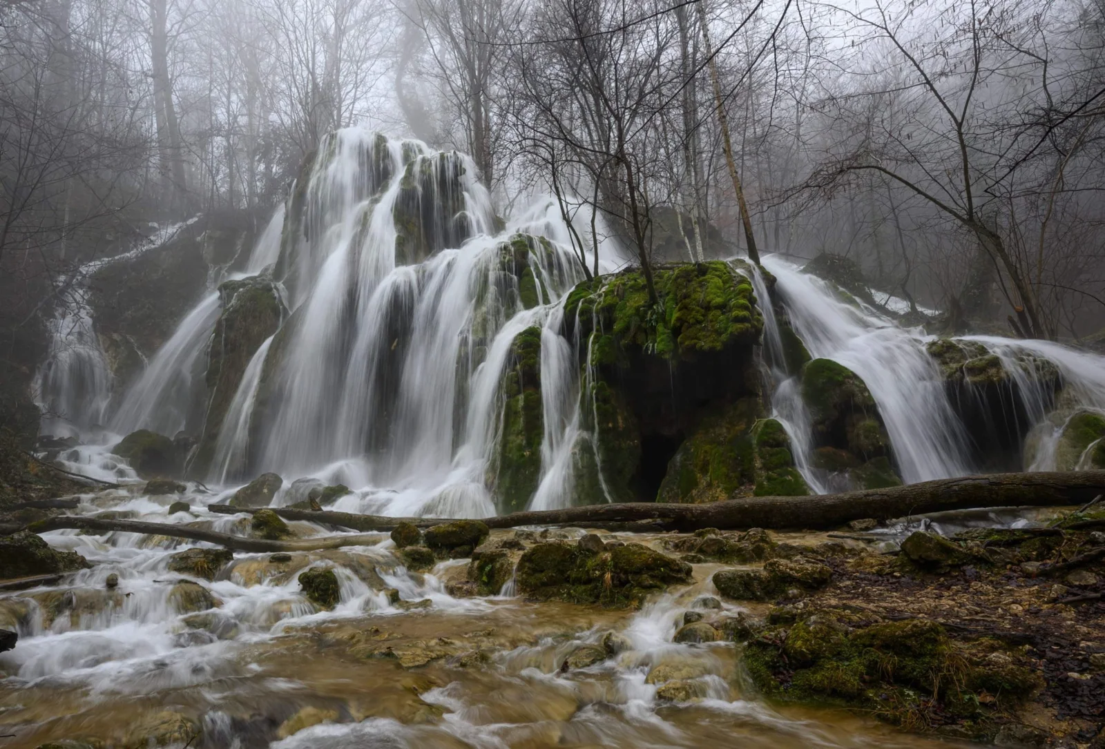 Beușnița waterfall flowing over broad mossy terraces in a misty forest